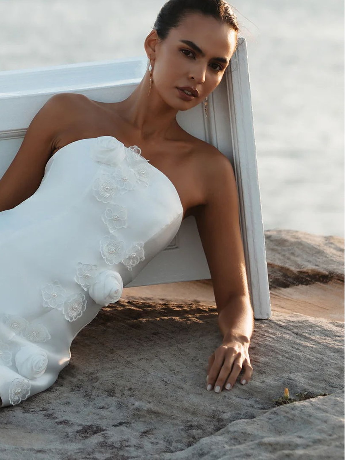 Model in a white strapless rosette mini dress leaning on a white plinth