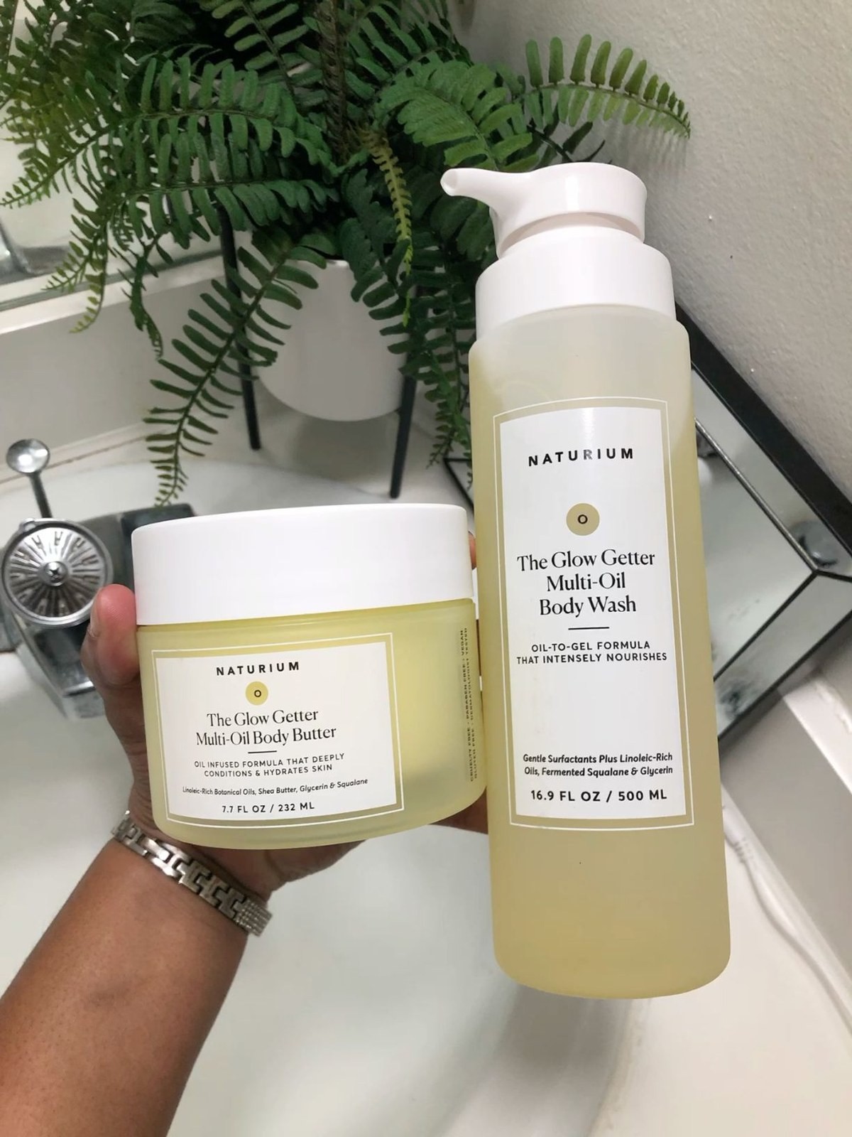 Hand holding the Naturium Glow Getter body butter and body wash in a bathroom