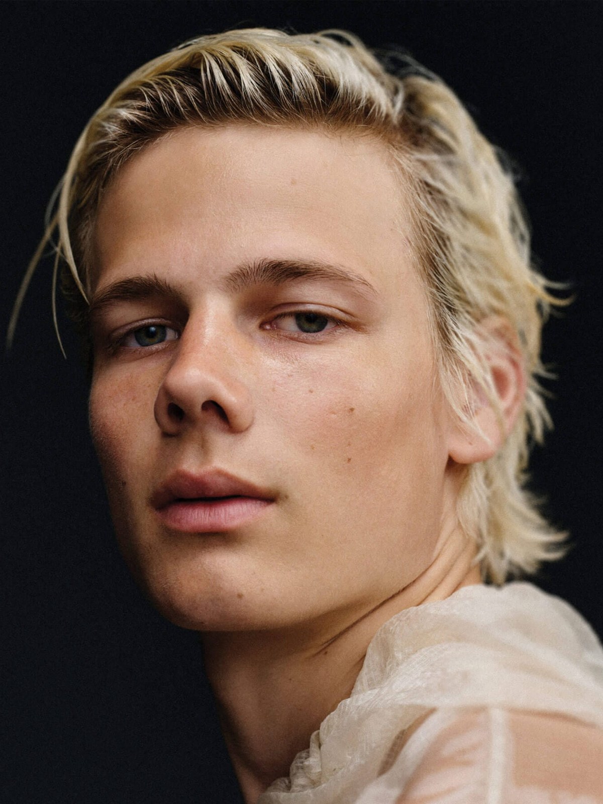 Blond model in a light shirt against a dark studio backdrop