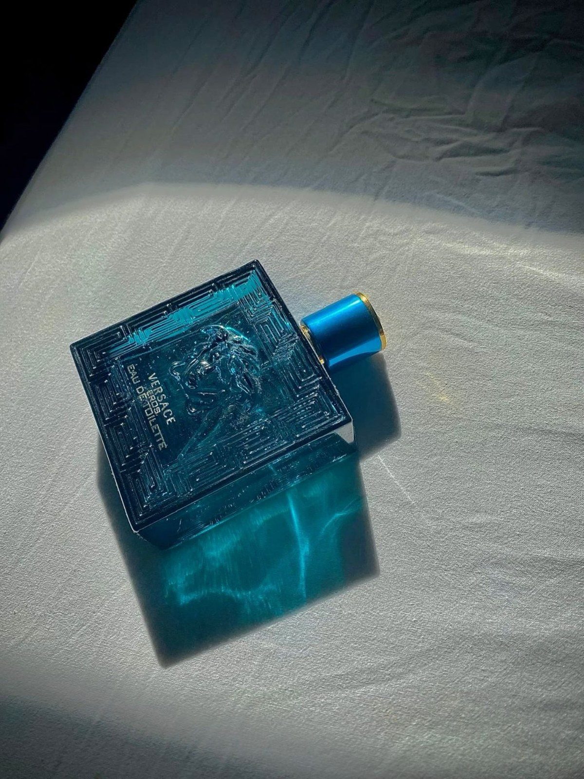 Hand holding a red Versace Eros Flame bottle over a sunlit wooden desk