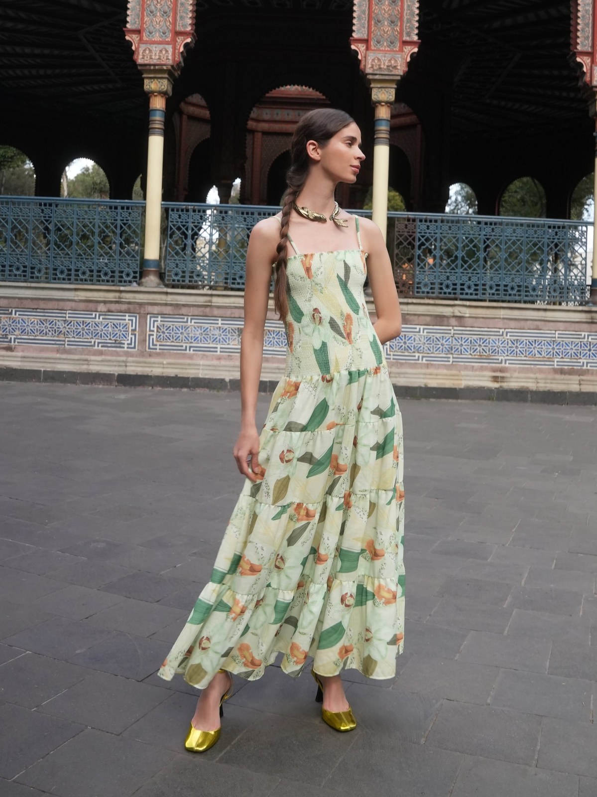 Model in a long green printed dress at an ornate courtyard