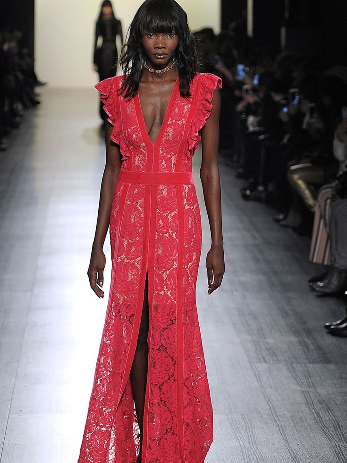 Runway model in a red lace gown with ruffled shoulders