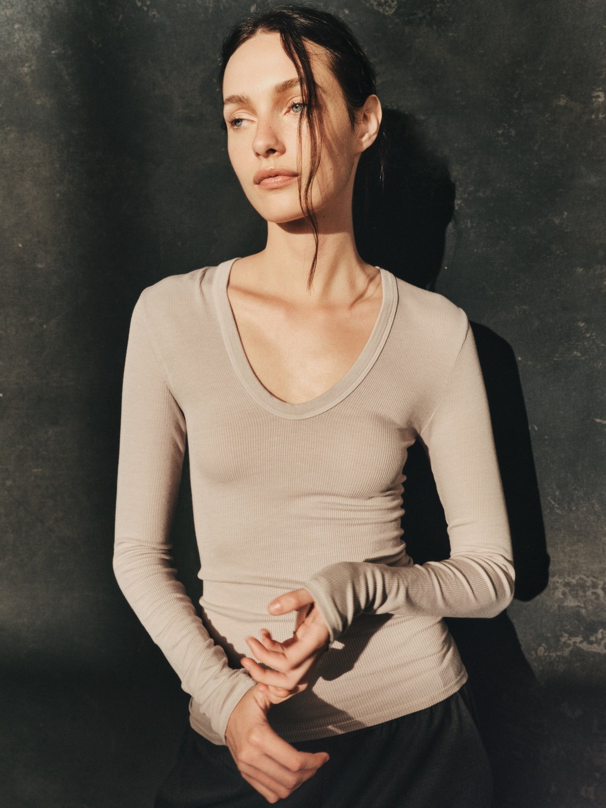 Model in a beige ribbed long sleeve against a dark studio backdrop