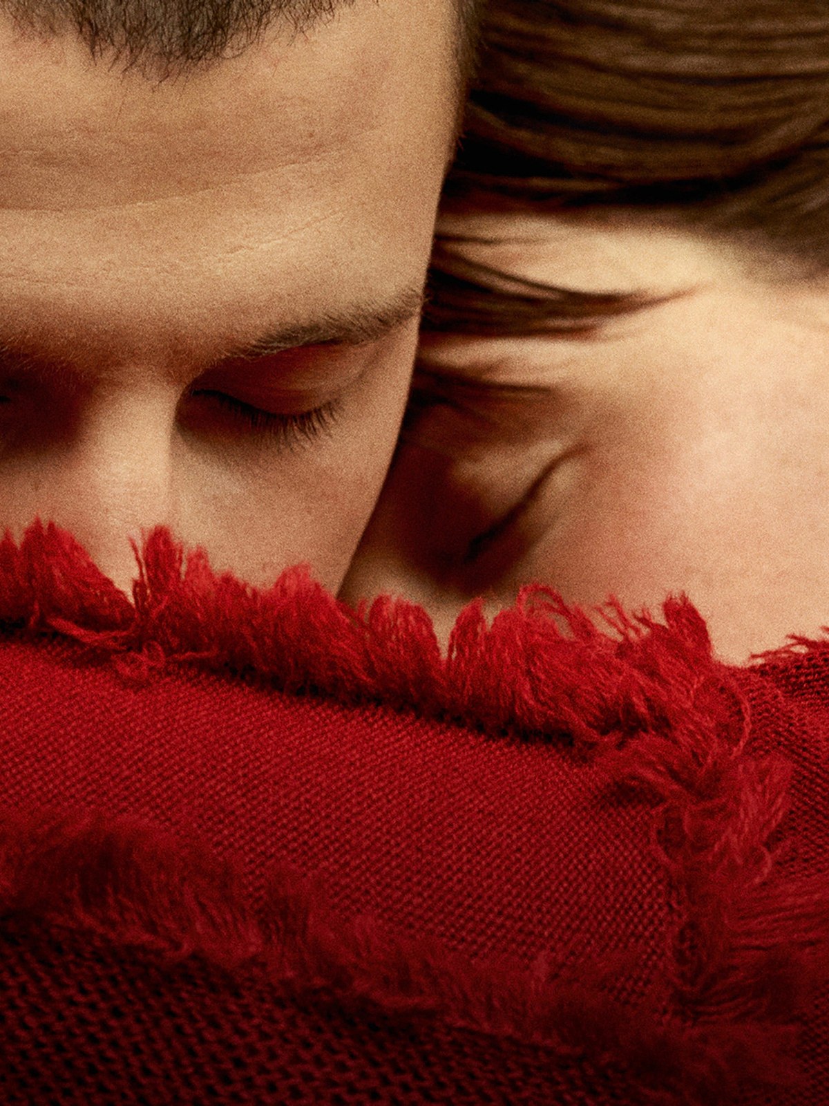 Two people in a close embrace wearing a red fringed knit