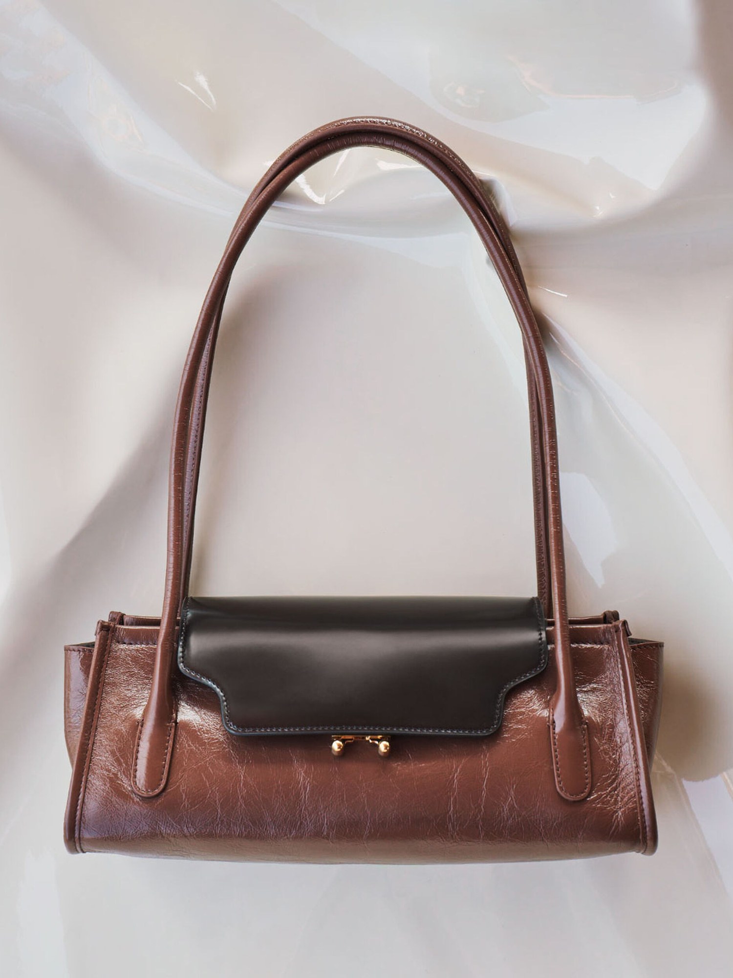 Brown leather shoulder bag with a dark flap on white satin