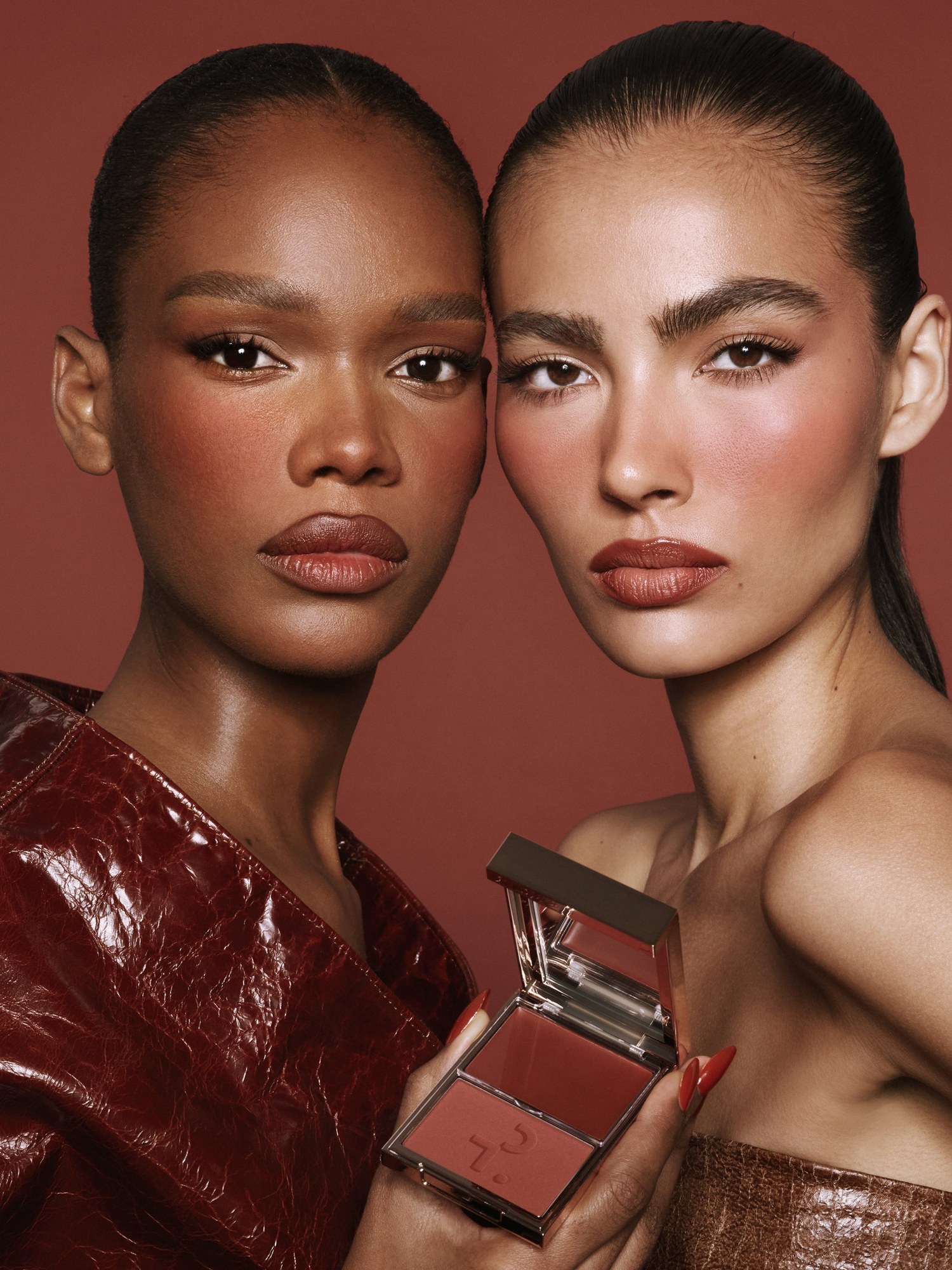 Two models with deep berry blush and lips, one in burgundy leather holding a blush duo compact