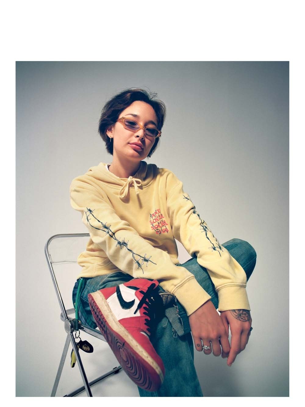 Woman lounging in a pale yellow sweatshirt and graphic pants with a sneaker