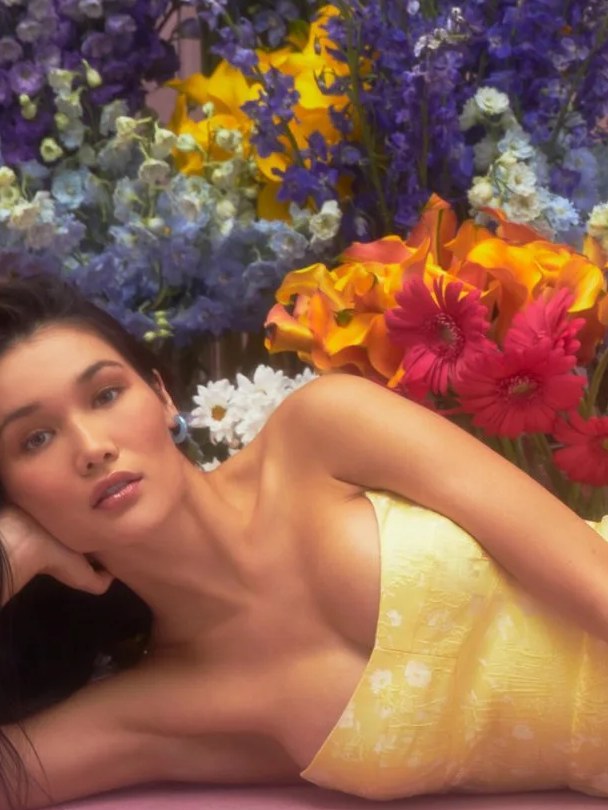 Model in a yellow dress reclining among bright spring flowers