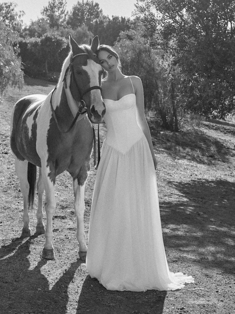Katie May bride beside a horse on a shaded path in a black and white campaign photo