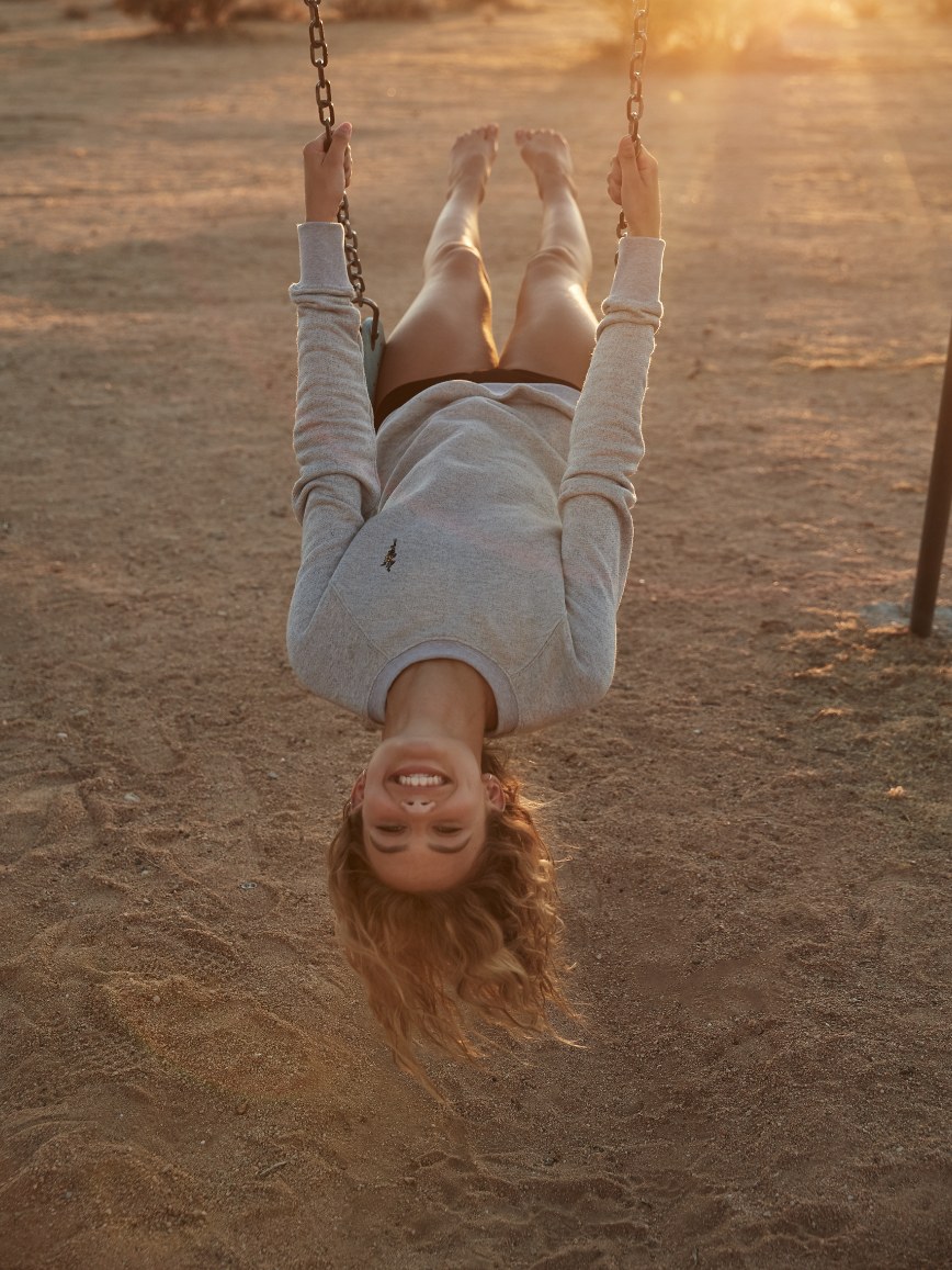 Woman smiling upside down on a swing at sunset
