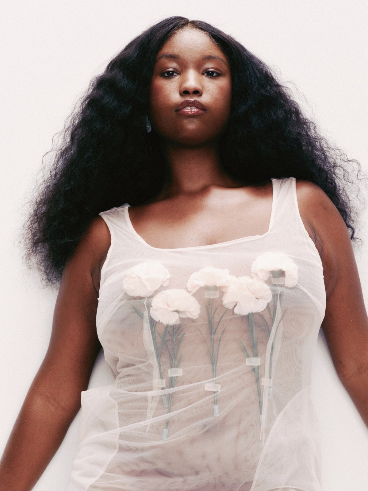 Black model in a sheer white top with floral appliques