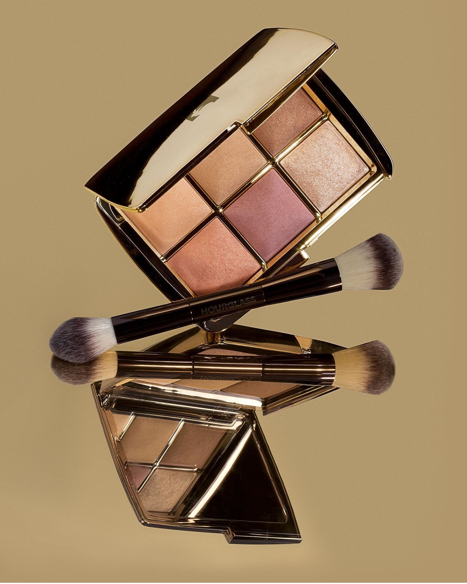 Two Hourglass Ambient Lighting palettes and makeup brushes on a gold background