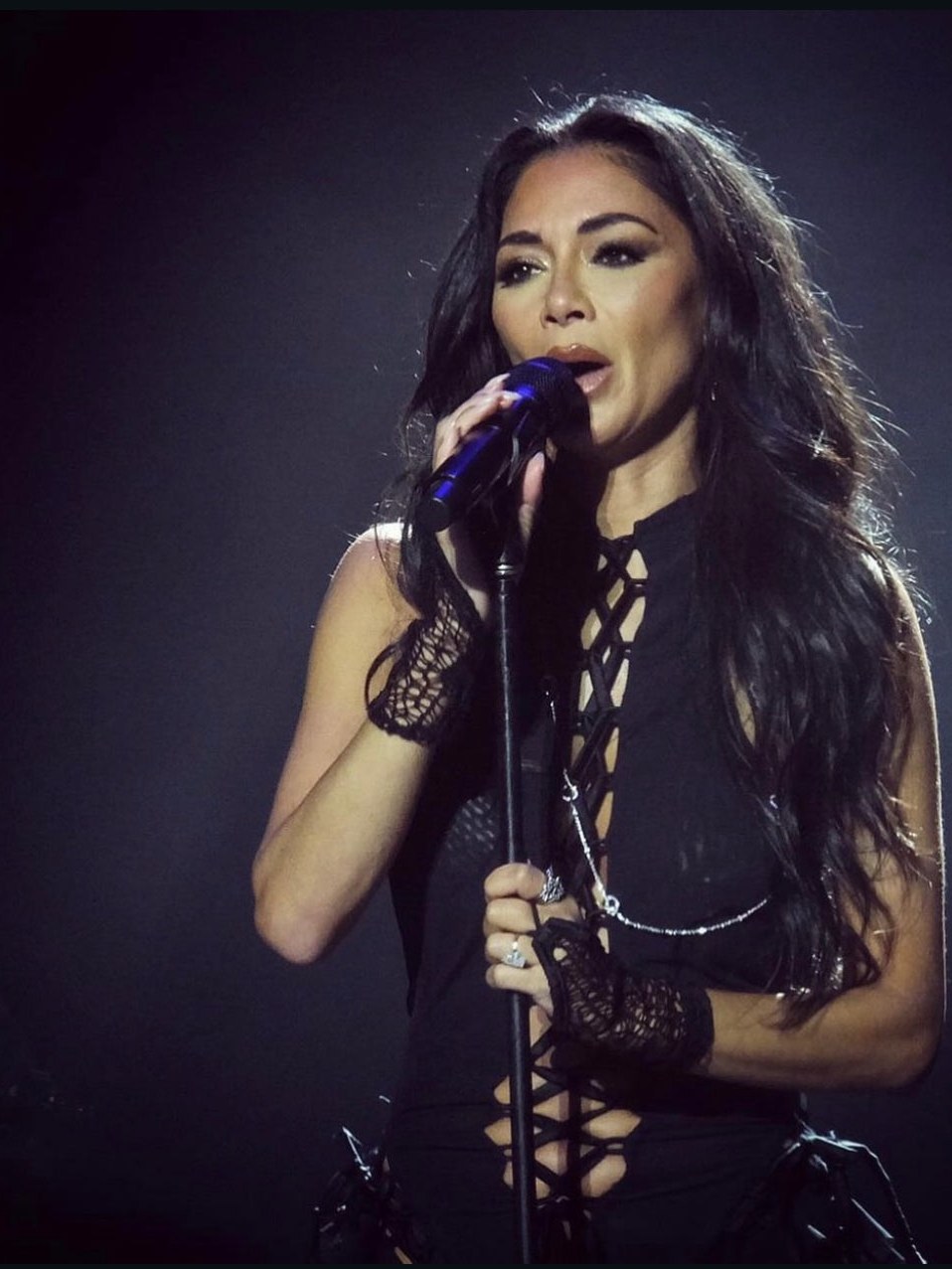 Nicole Scherzinger singing in a black lace-up AMOR MIA jumpsuit