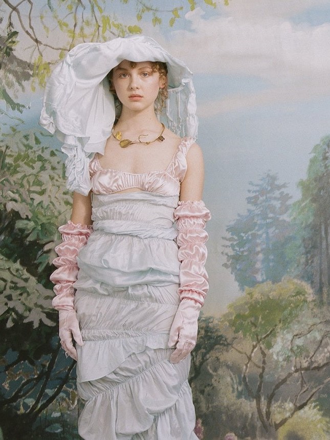 Model in a pale tiered dress against a painted landscape