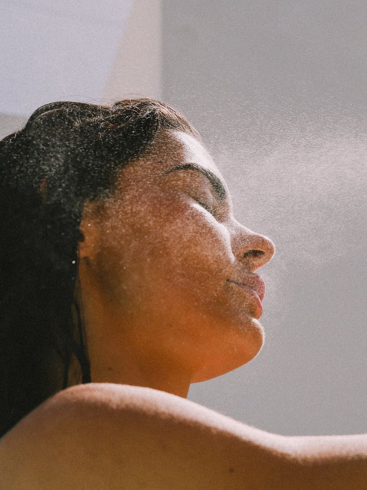 Woman with wet hair leaning back into a backlit mist of water droplets
