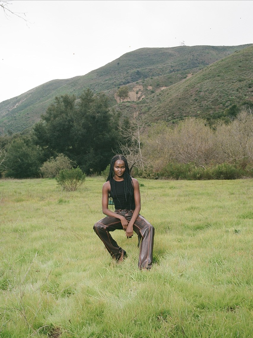 Model seated in a field with hills behind her