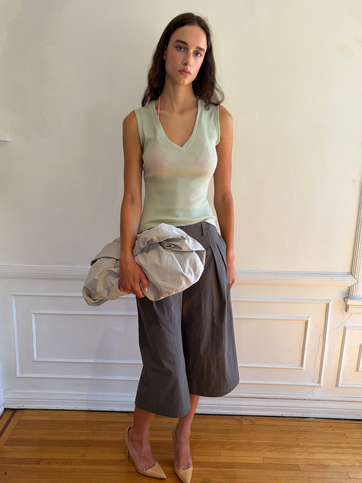 Model in a mint sleeveless top and taupe trousers seated in a sunlit room with a silver bag