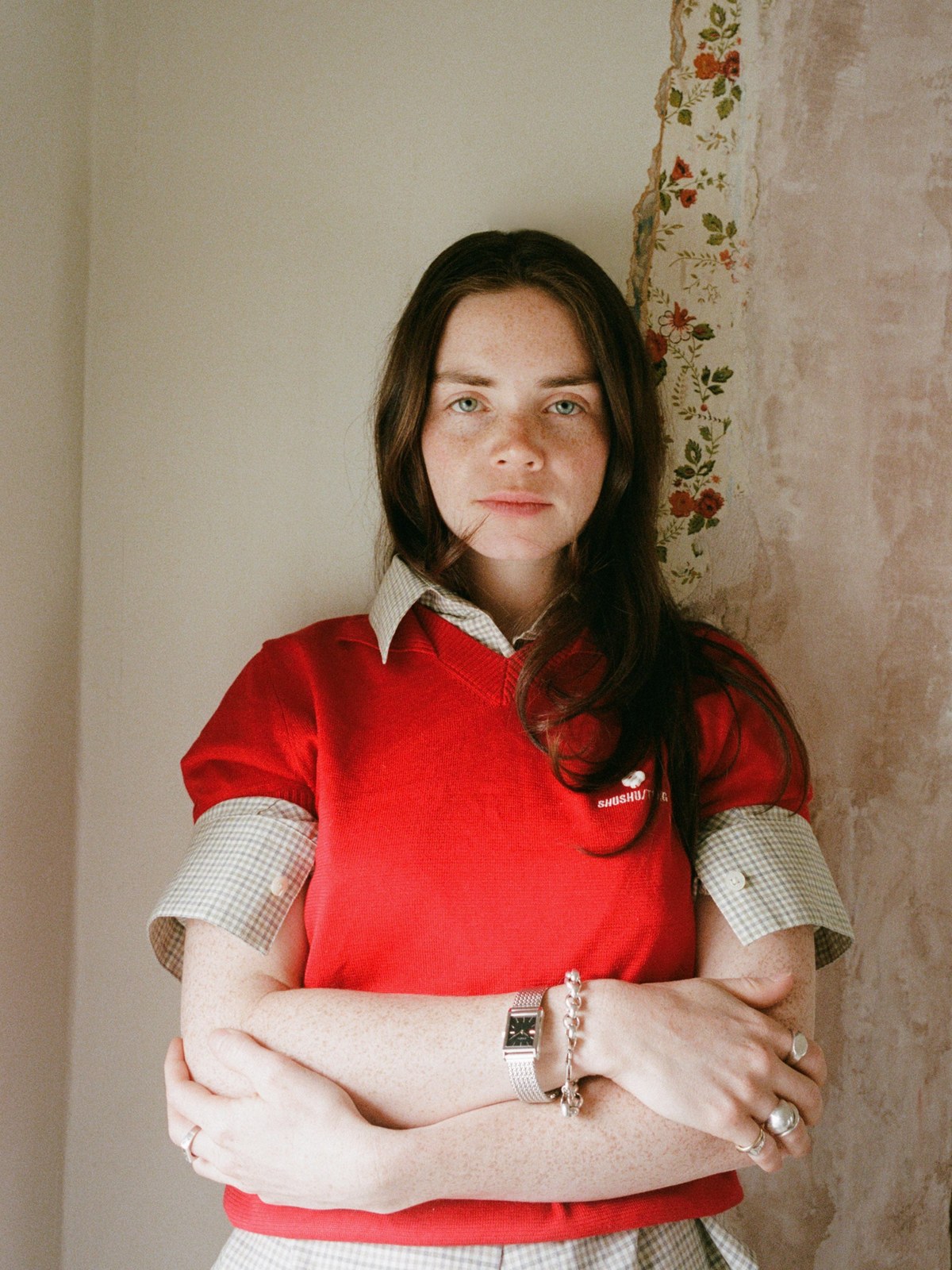 Woman in a red shirt wearing a silver watch against a pale wall