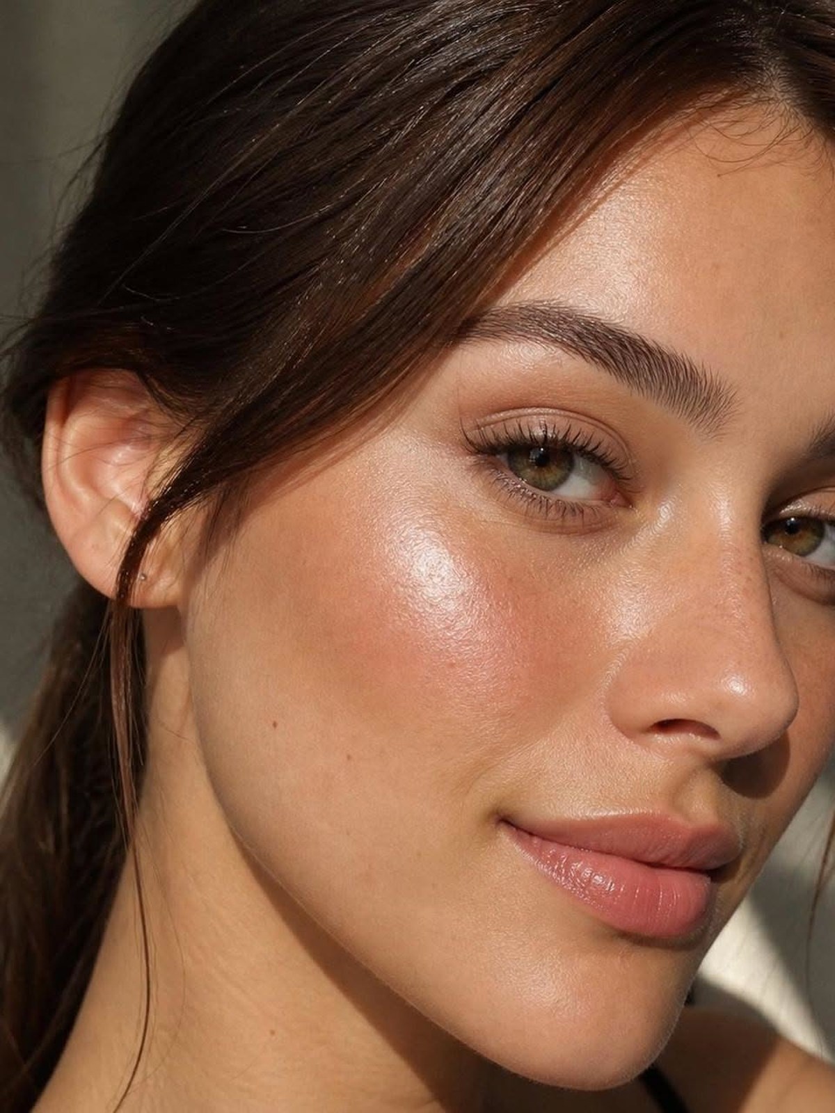 Close-up of a woman with dark hair and a soft glowing, dewy cheek in warm light
