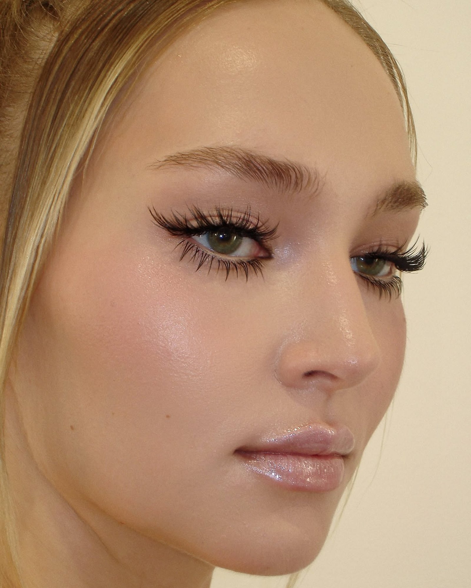 Close-up of a blonde woman's eye with dark, feathery lashes and glossy lips
