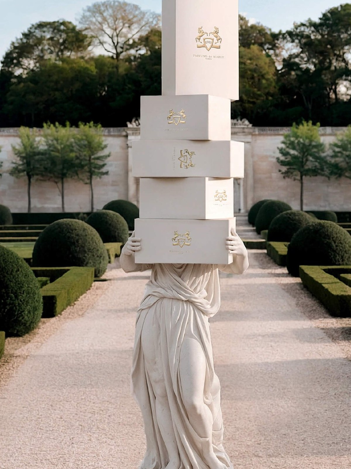 Classical statue carrying a stack of white boxes down a formal garden path