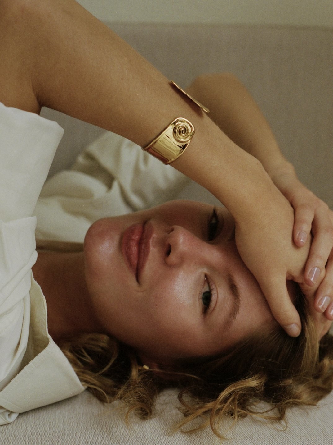 Model reclining in a white blouse wearing a gold ANNI LU bracelet