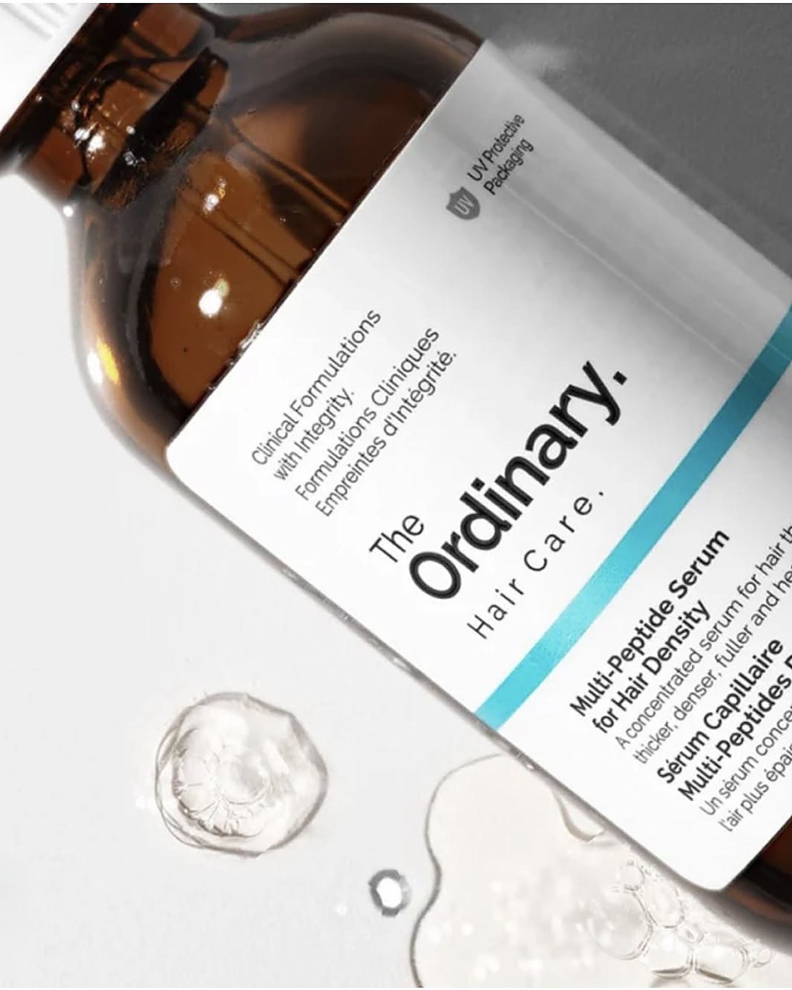 Close-up of a brown glass bottle of The Ordinary Multi-Peptide Serum for Hair Density with drops of clear serum beside it