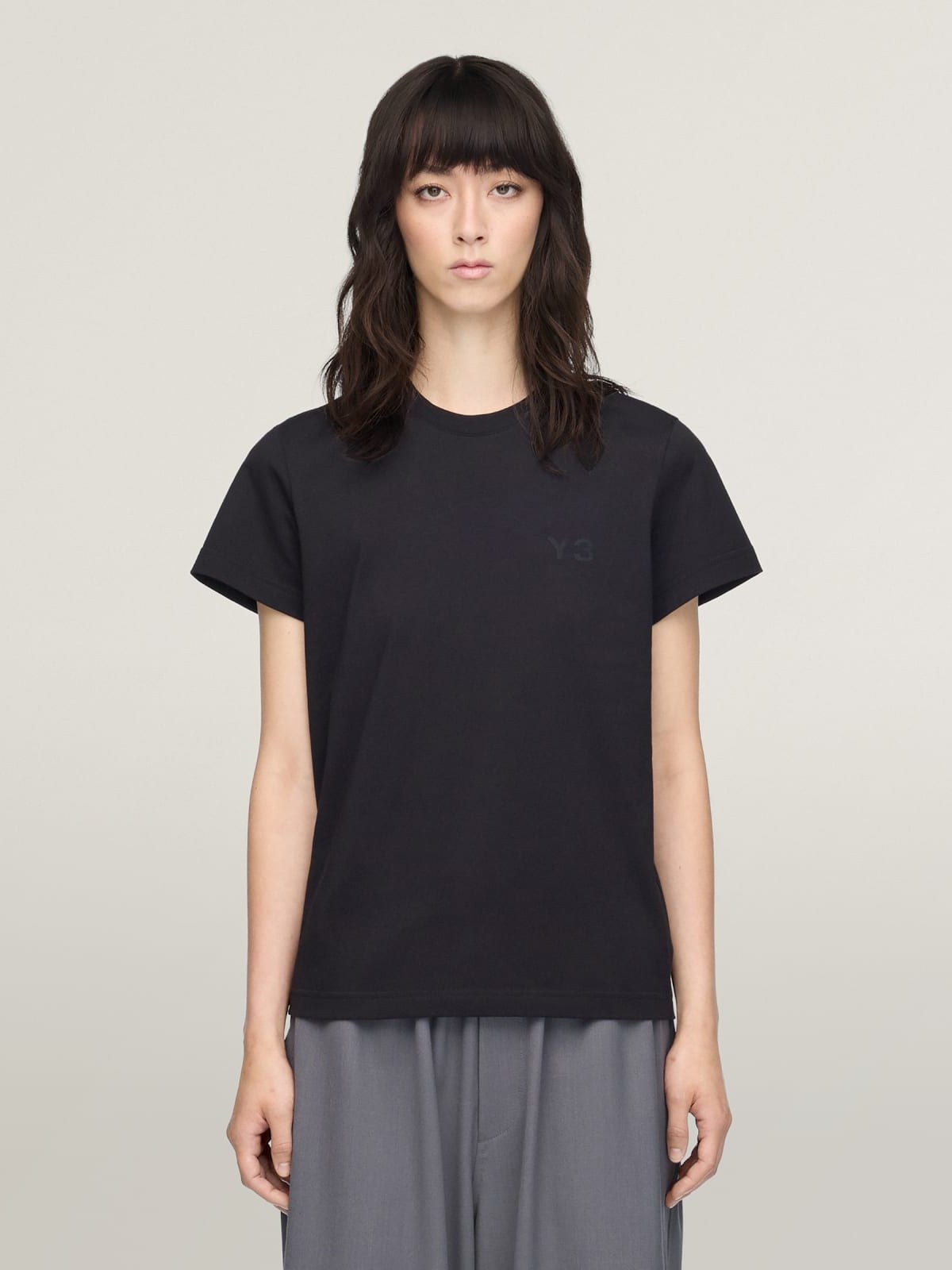 Model with bangs in a black tee and grey wide trousers