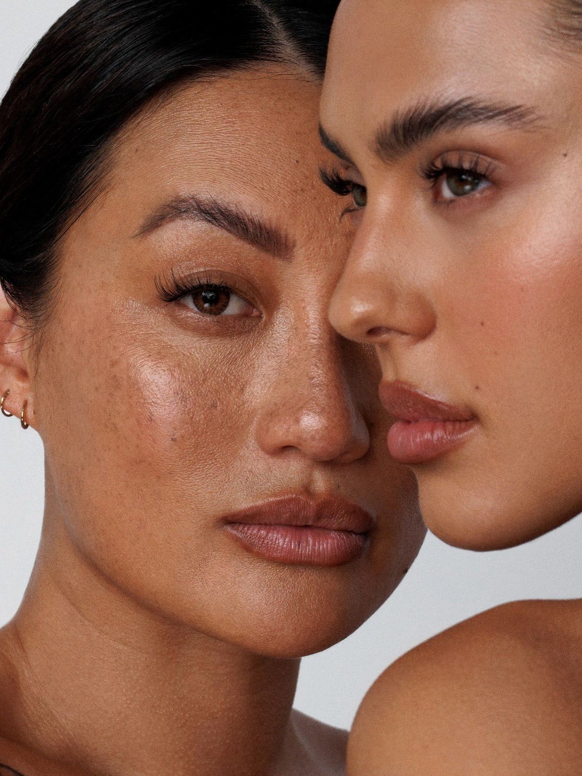 Two women's faces close together showing natural lashes and defined brows