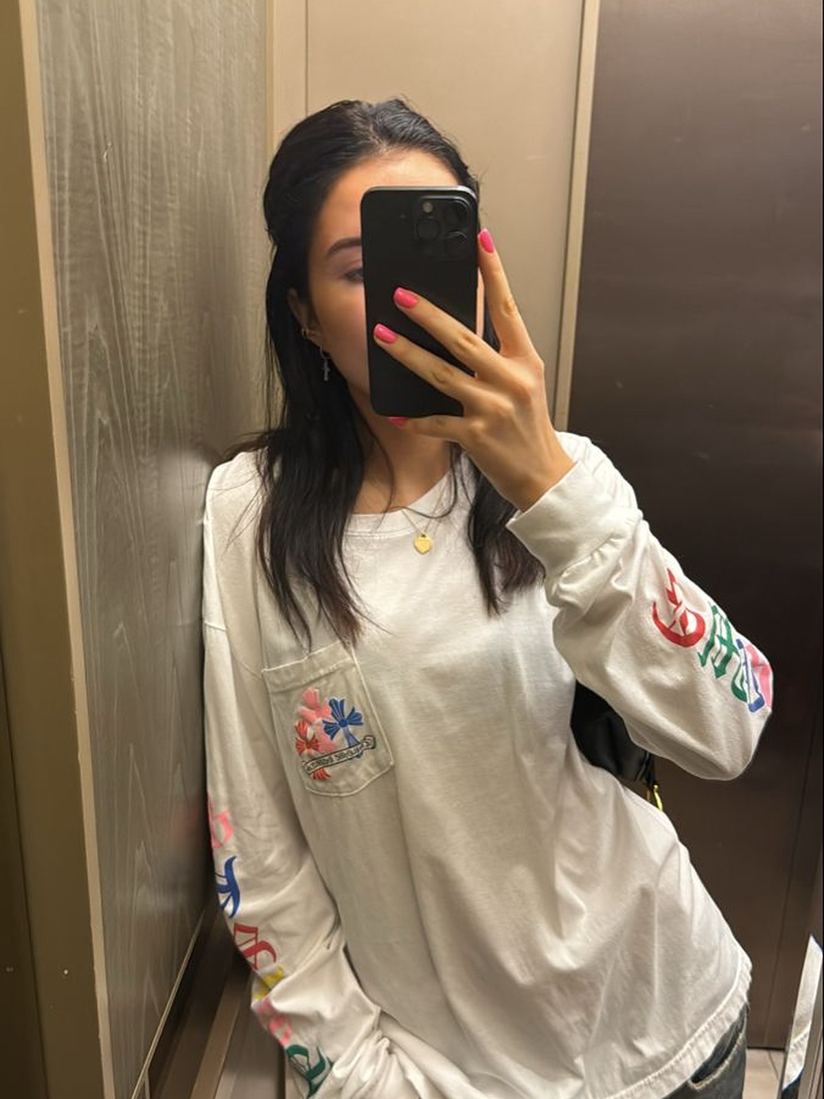 Woman in a white long sleeve top with colorful cross details taking a mirror photo