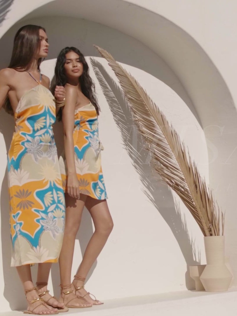 Two models in colorful MISA dresses beneath a white arch