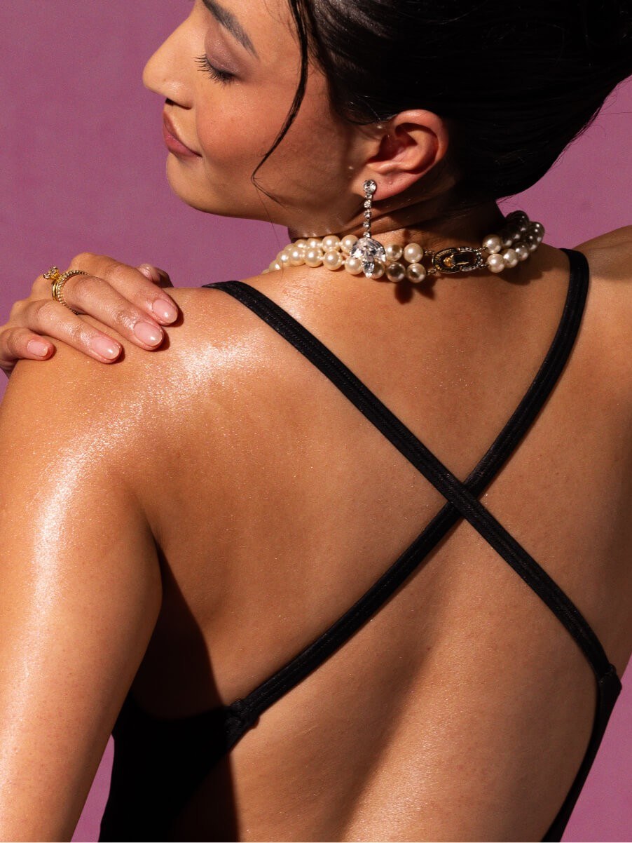 Model in a black strappy swimsuit and pearl jewelry against a rose backdrop