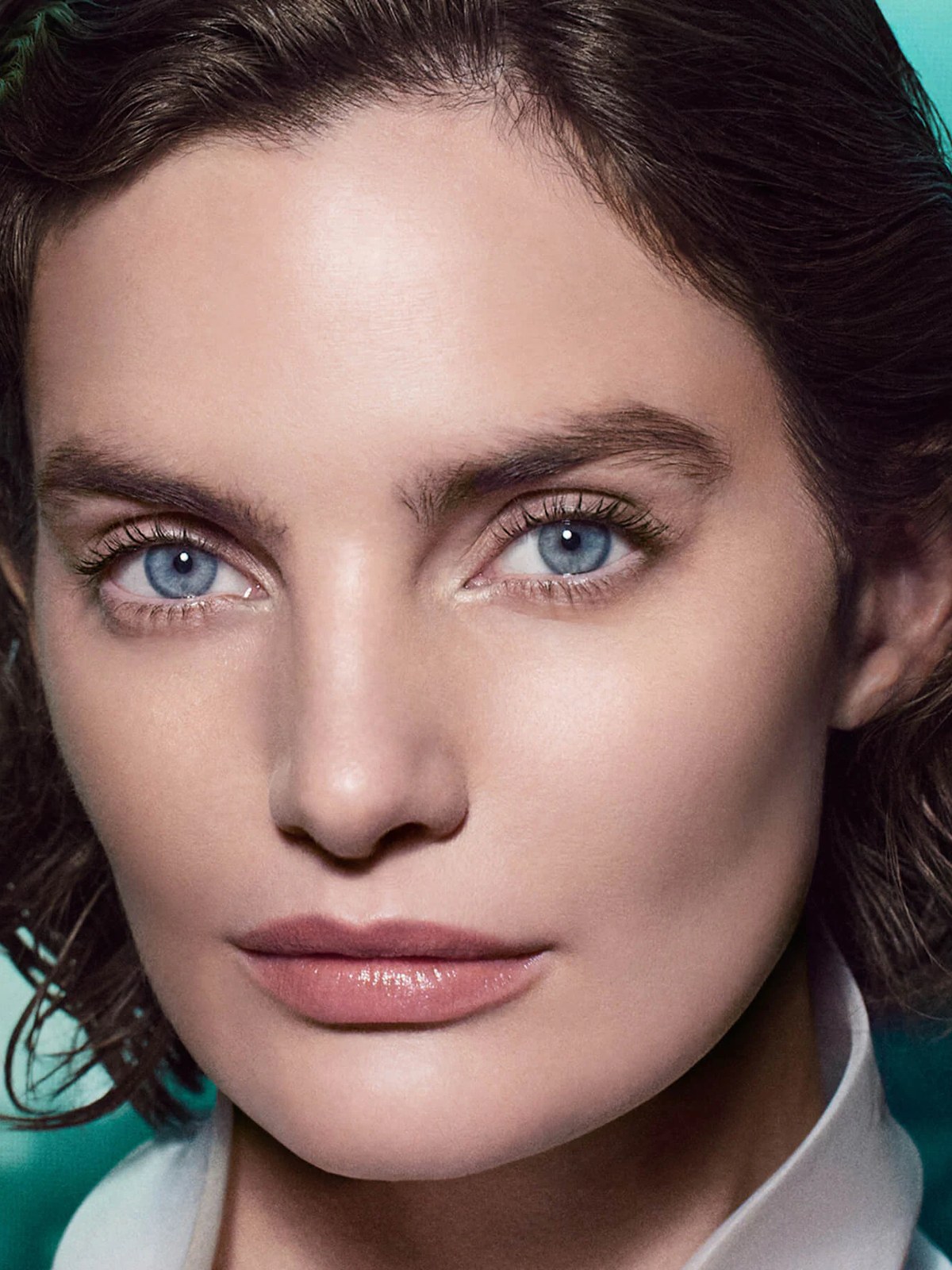 Close up portrait of a model with glowing skin against a teal background
