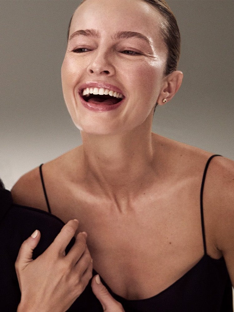 A laughing woman in a black top with a companion's hand at her shoulder