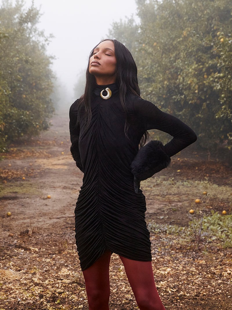 Woman in a black dress with gold hoop jewelry standing among trees