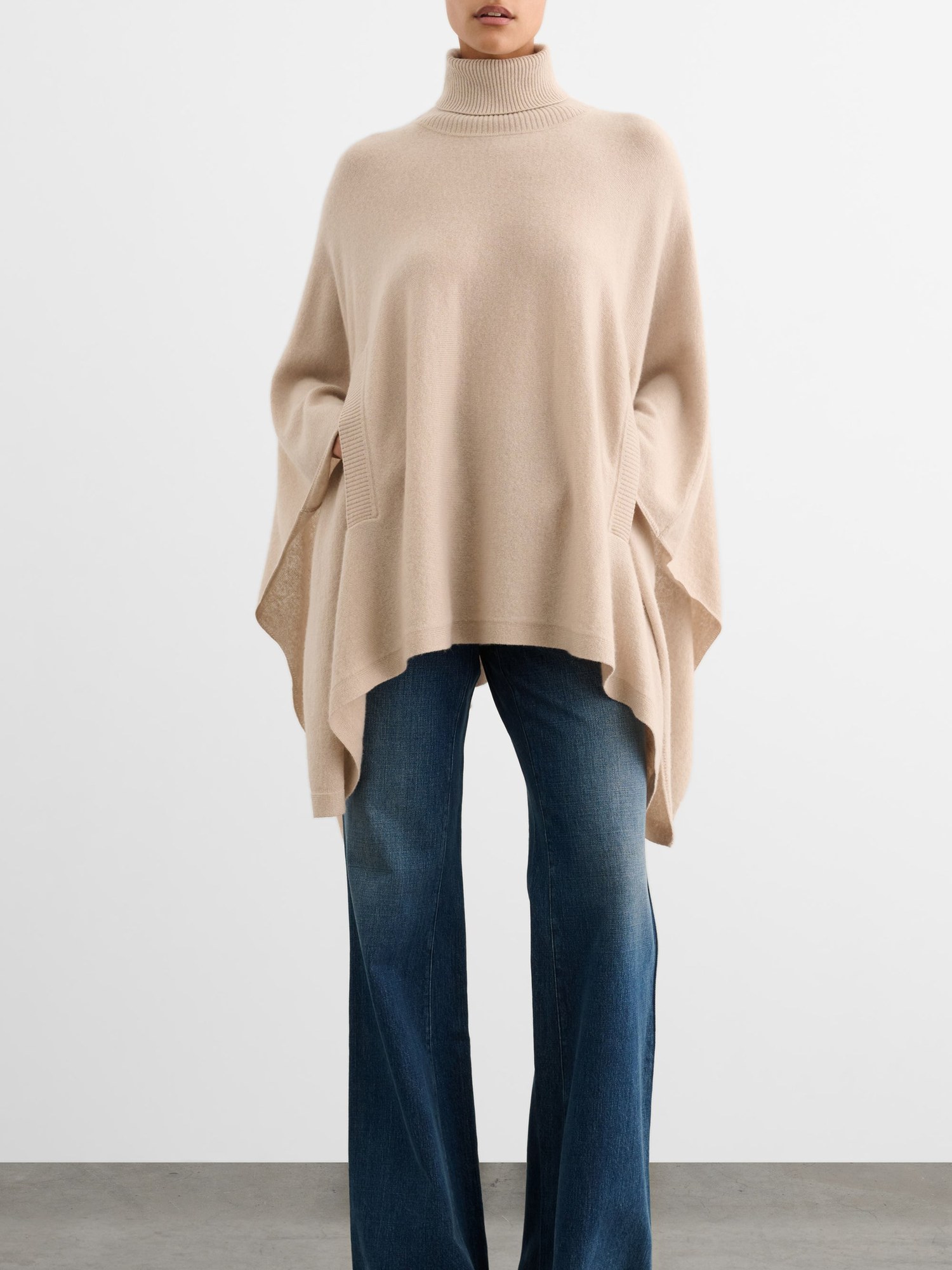 Model in a cream poncho style knit and wide leg jeans