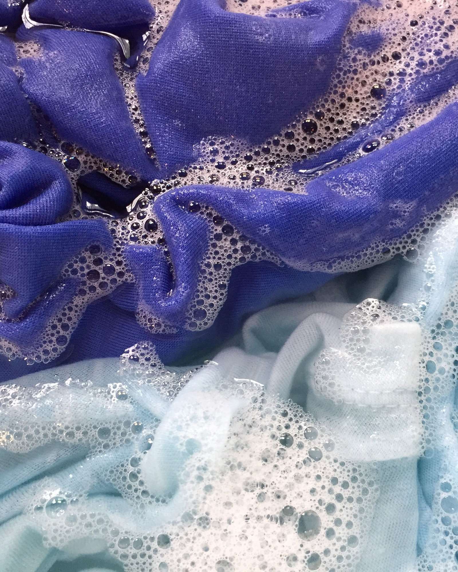 Violet and pale blue fabric soaking in soapy water under a layer of bubbles