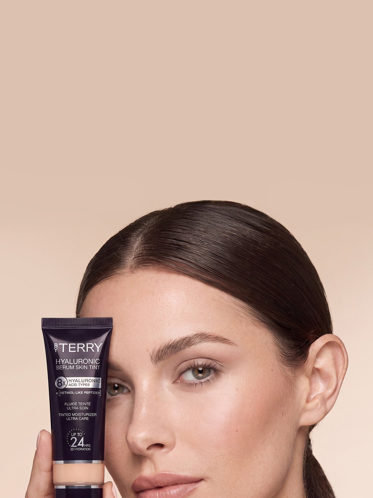 Model holding a complexion product against a warm beige studio background