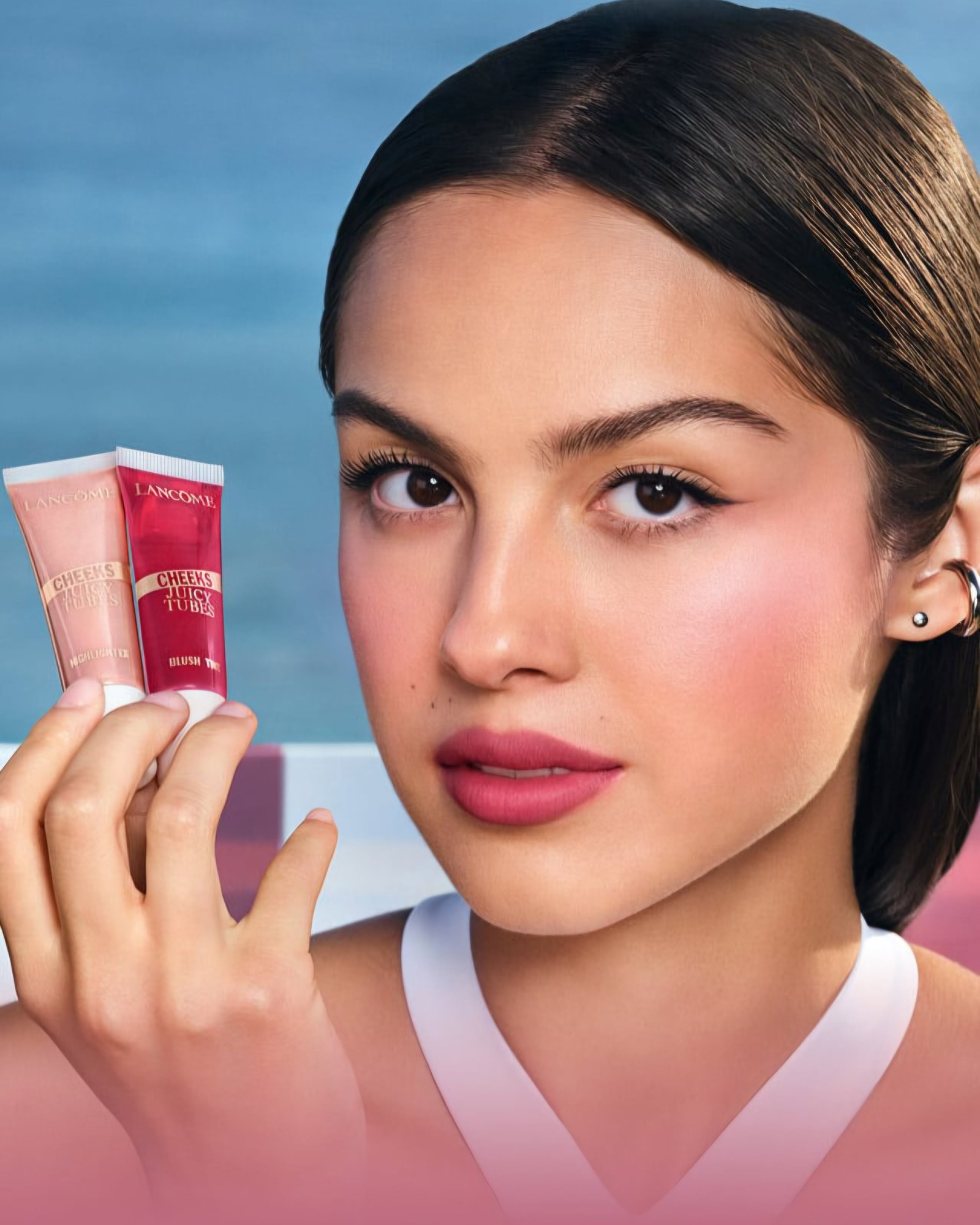 Woman with a sleek dark ponytail and pink blush holding two Lancôme Cheeks Juicy Tubes in pink and red by her face