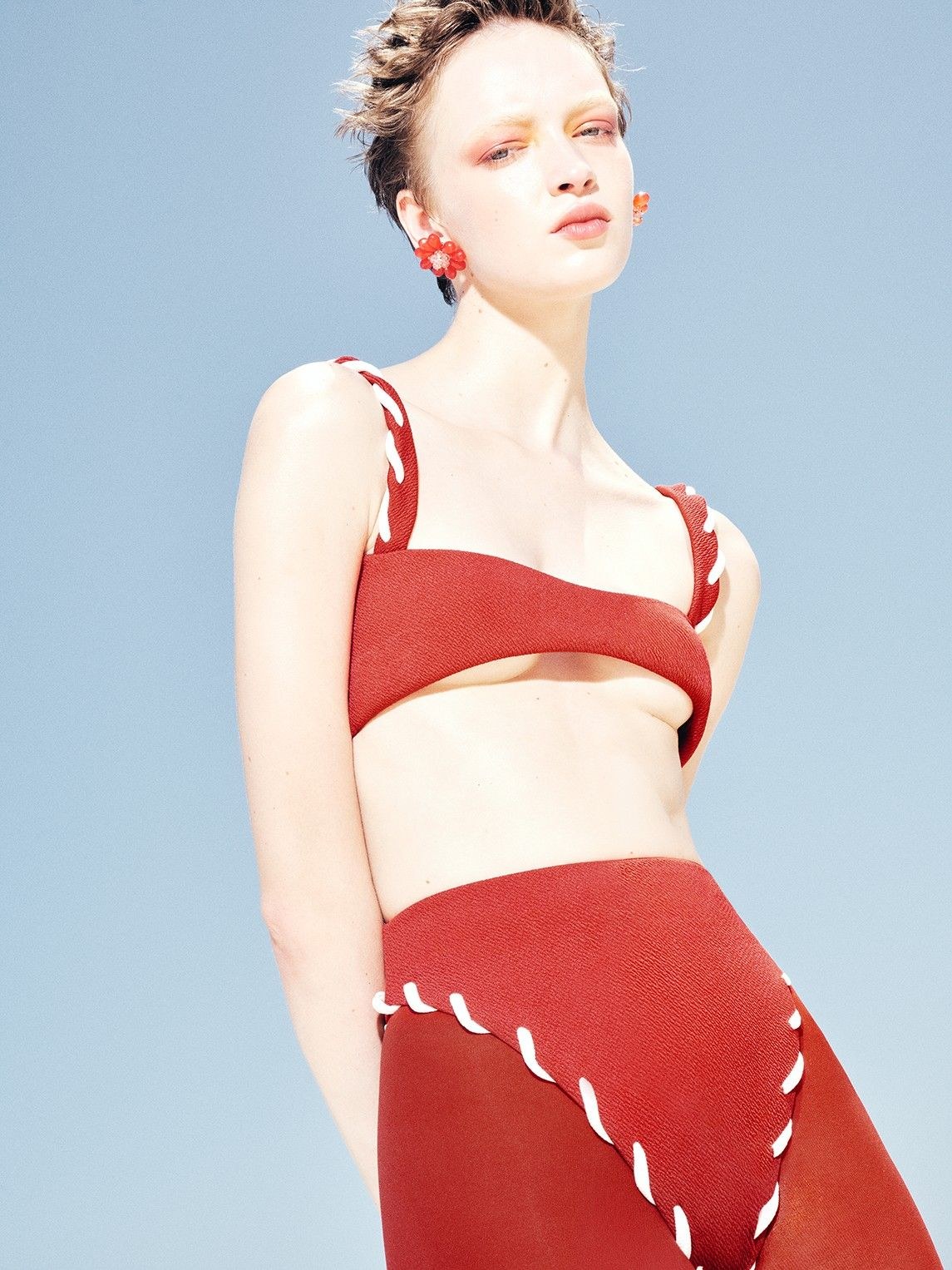 Model in a red Nau swimsuit with white trim against a light blue background