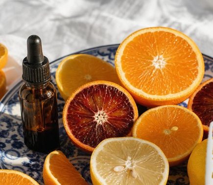 Collage on an off-white page showing the Sunday Riley C.E.O. 15% Vitamin C Brightening Serum and the Summer Fridays CC Me Vitamin C + Niacinamide Serum, with six more picks from this edit, beside a still-life photo of sliced oranges and blood oranges on a blue and white plate with a dropper bottle.