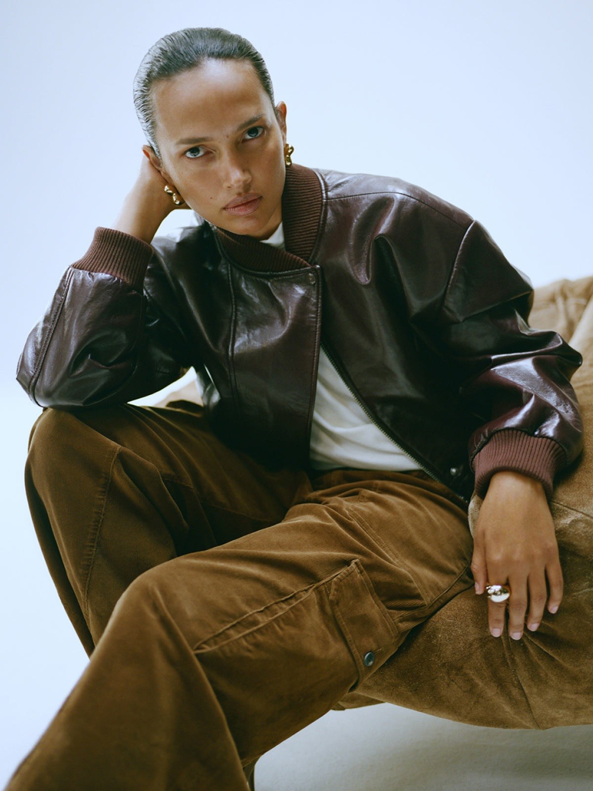 Woman seated in a brown leather jacket and brown corduroy trousers by Citizens of Humanity