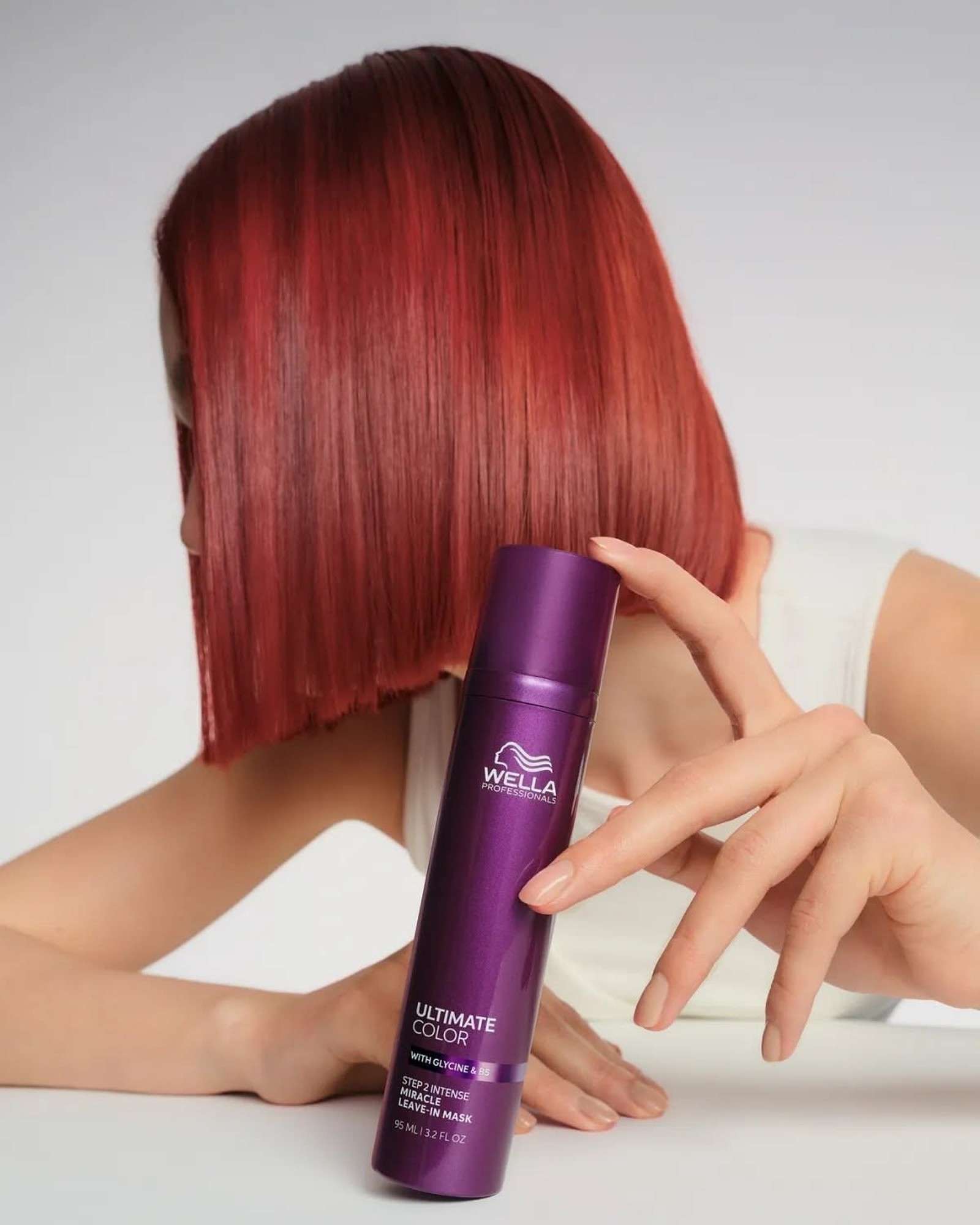 Woman with a sleek red bob holding a purple Wella Ultimate Color Miracle Leave-In Mask bottle