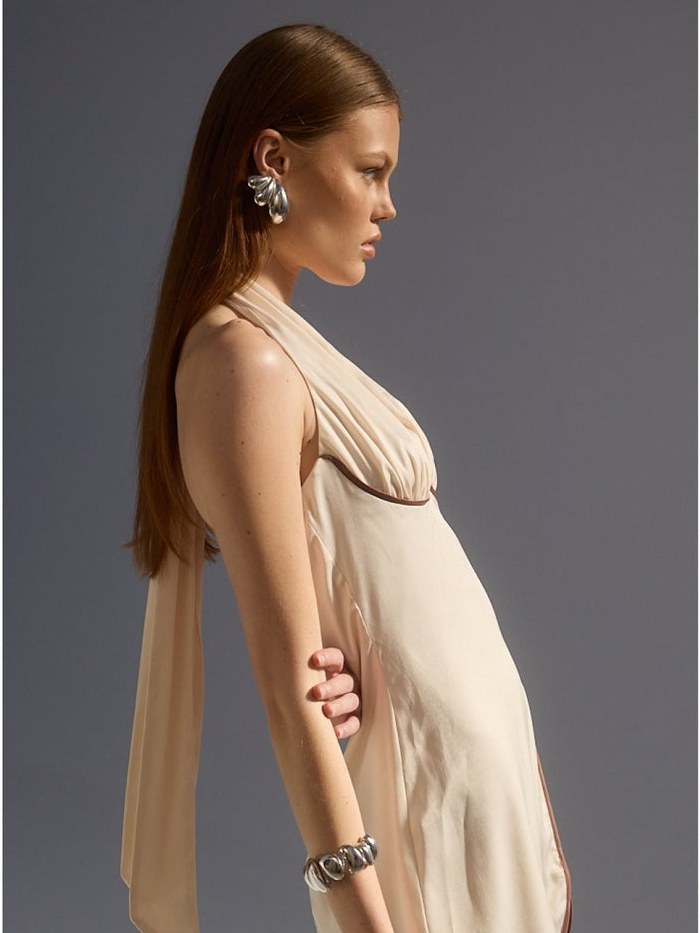Model in a pale satin dress, shown in profile against a charcoal backdrop
