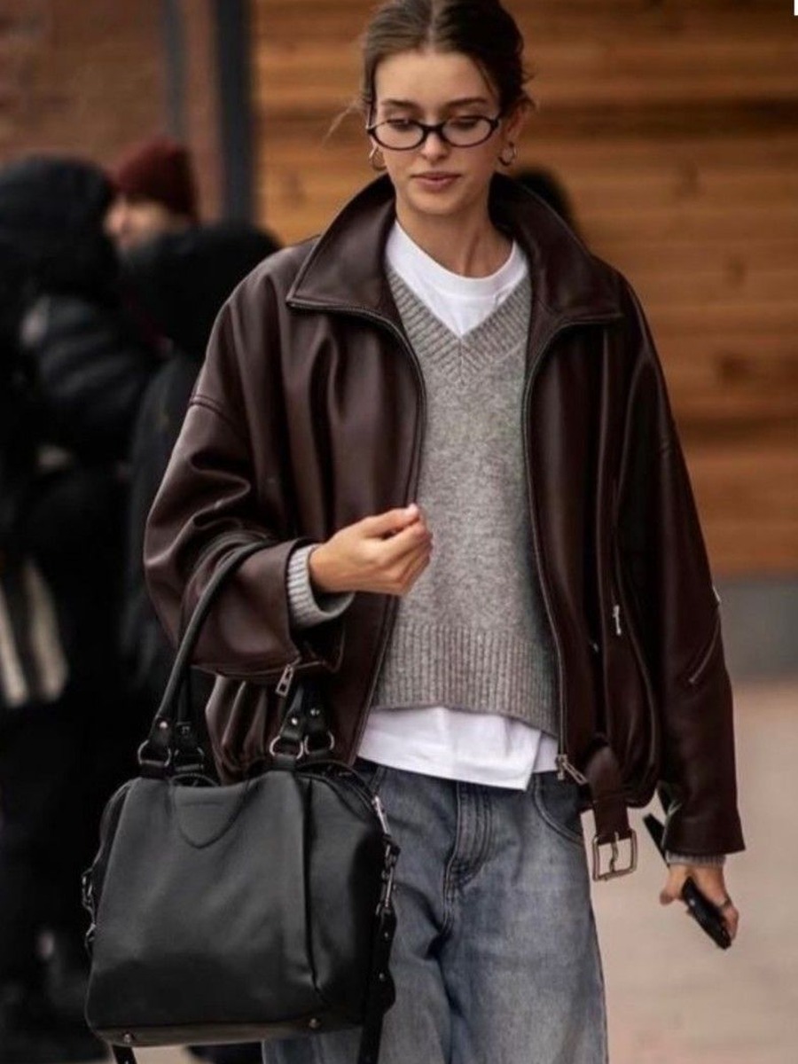 Street style photo of a woman in a brown leather jacket over a grey knit vest and jeans