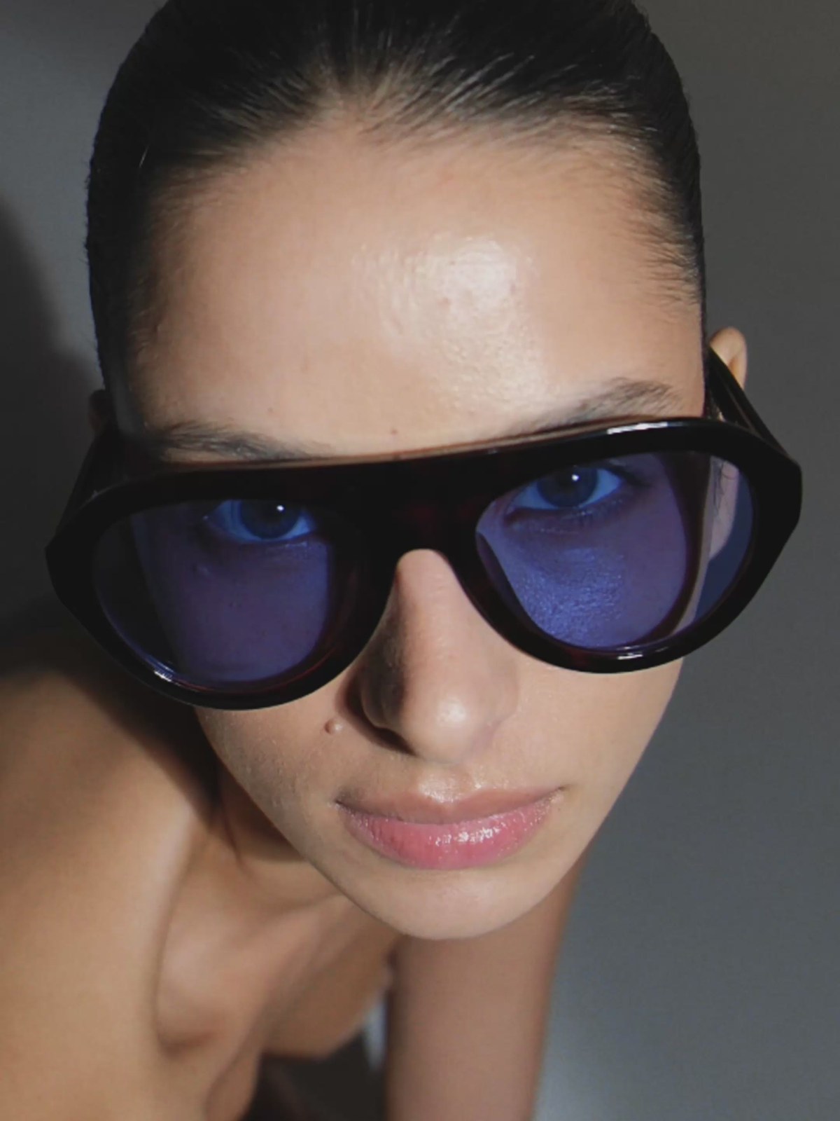 Close portrait of a model in blue-tinted black sunglasses against a dark studio background