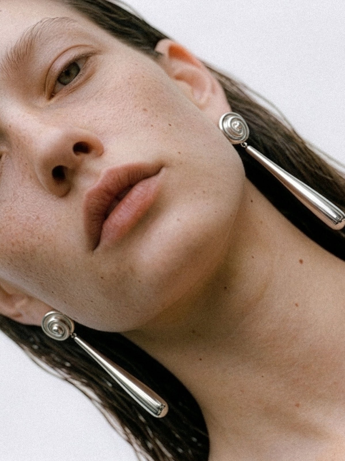 Model wearing a silver drop earring in a close, tilted studio portrait