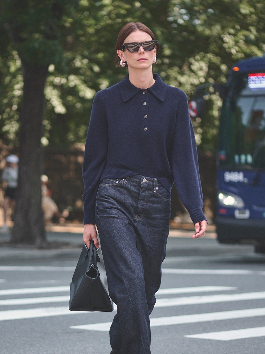 Model in a navy polo and dark trousers walking on a city street