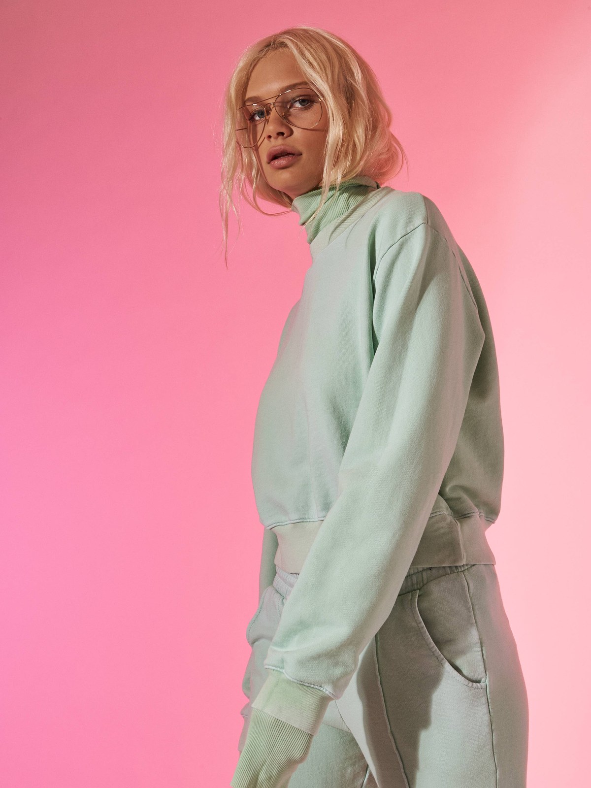 Model wearing a mint sweatshirt and matching joggers against a pink studio backdrop