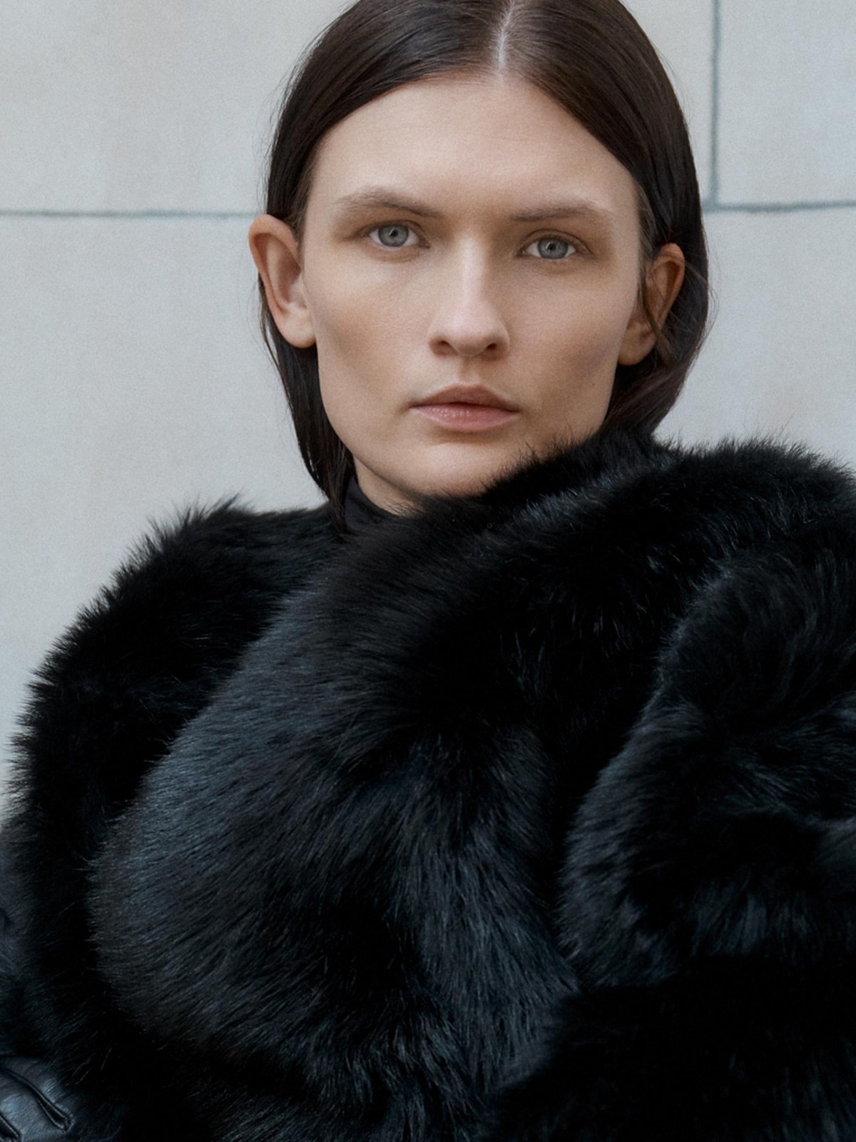Close portrait of a model in dramatic black textured outerwear against pale stone